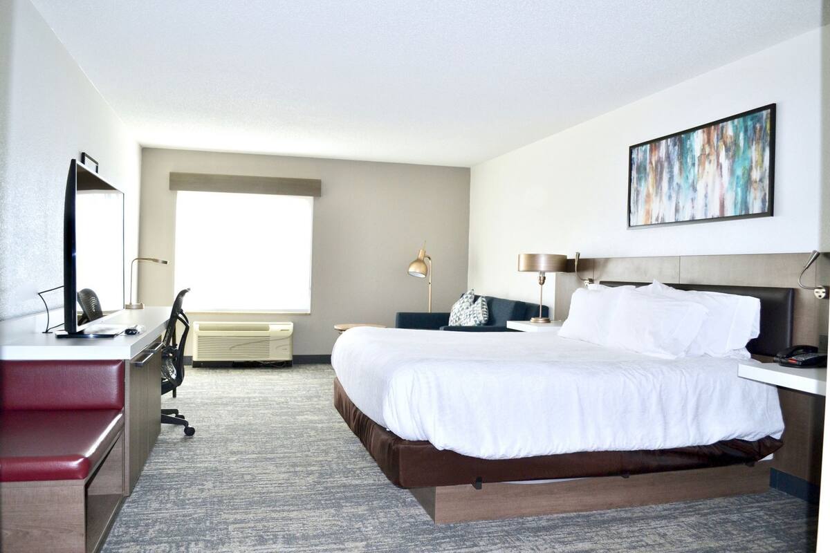 Una habitación de hotel con cama, escritorio, silla y un ventanal grande.