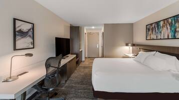 A hotel room with a bed, desk, chair, TV, and artwork on the walls.