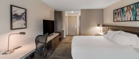 A hotel room with a bed, desk, chair, TV, and artwork on the walls.