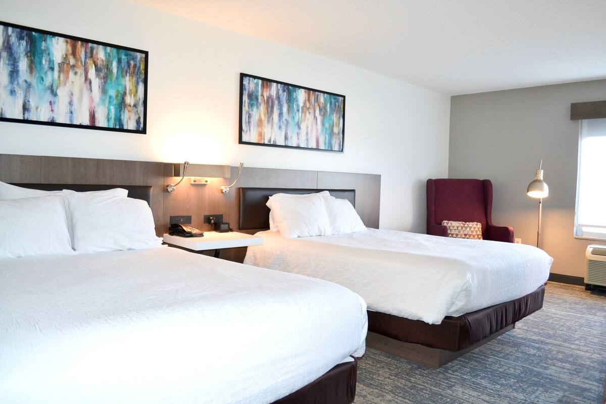 A hotel room with two beds, a desk, a chair, and artwork on the walls.