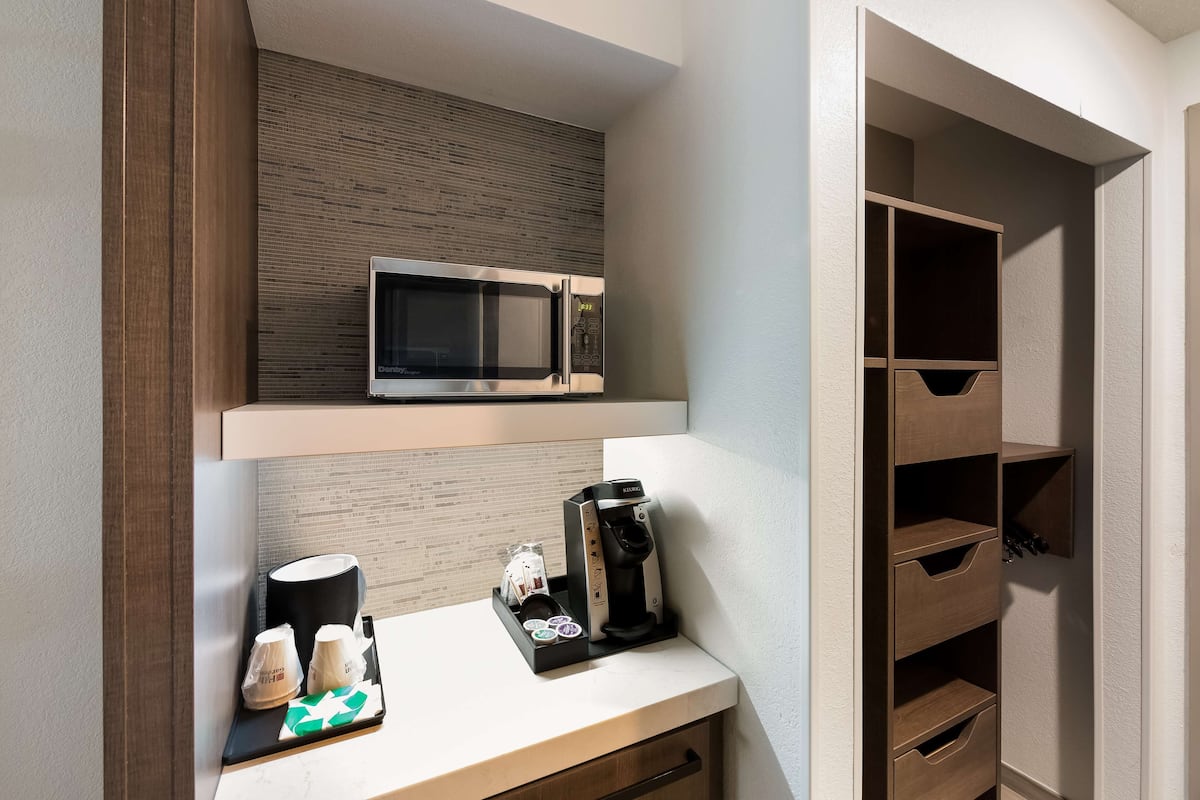 A kitchenette with a microwave, coffee maker, and coffee pods on a countertop.