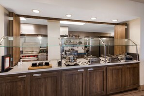 A buffet area with a glass partition, stainless steel appliances, and wooden cabinets. - Hilton Garden Inn Columbus/Grove City (Grove City)