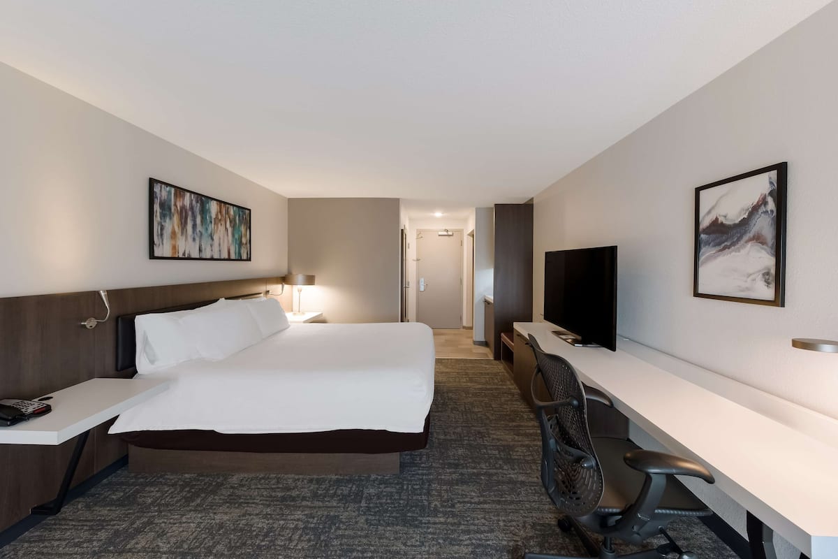 A hotel room with a bed, desk, chair, TV, and artwork on the walls.