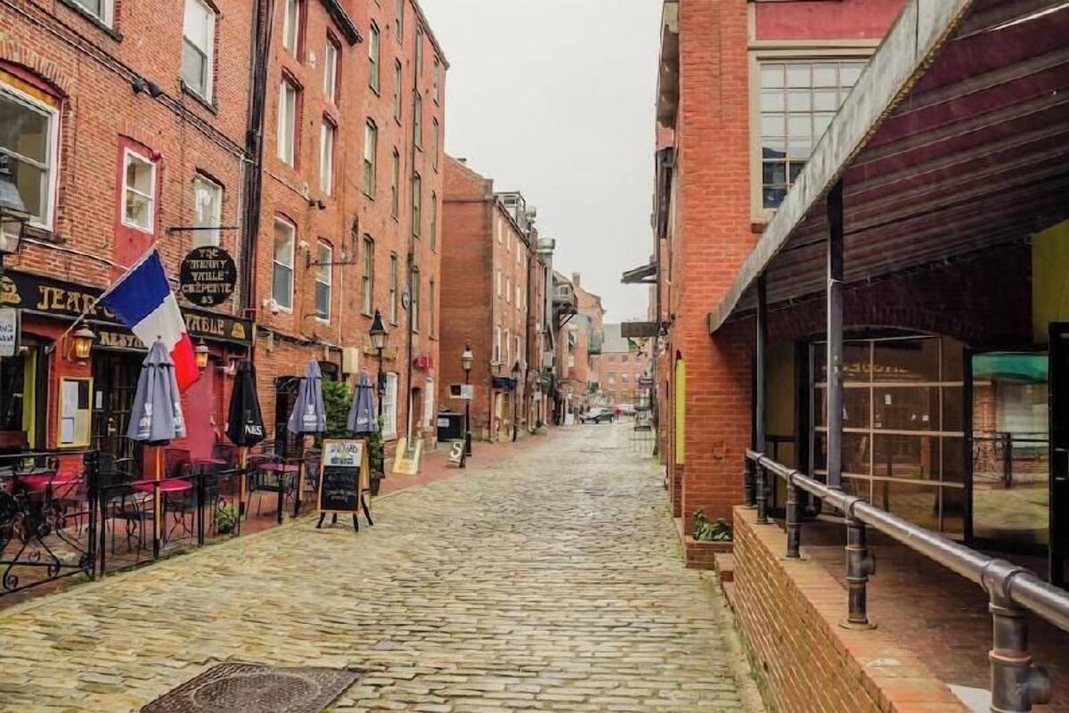 A cobblestone street lined with brick buildings, outdoor seating, and a mix of storefronts.