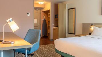 A hotel room with a bed, desk, chair, lamp, and a mirror.