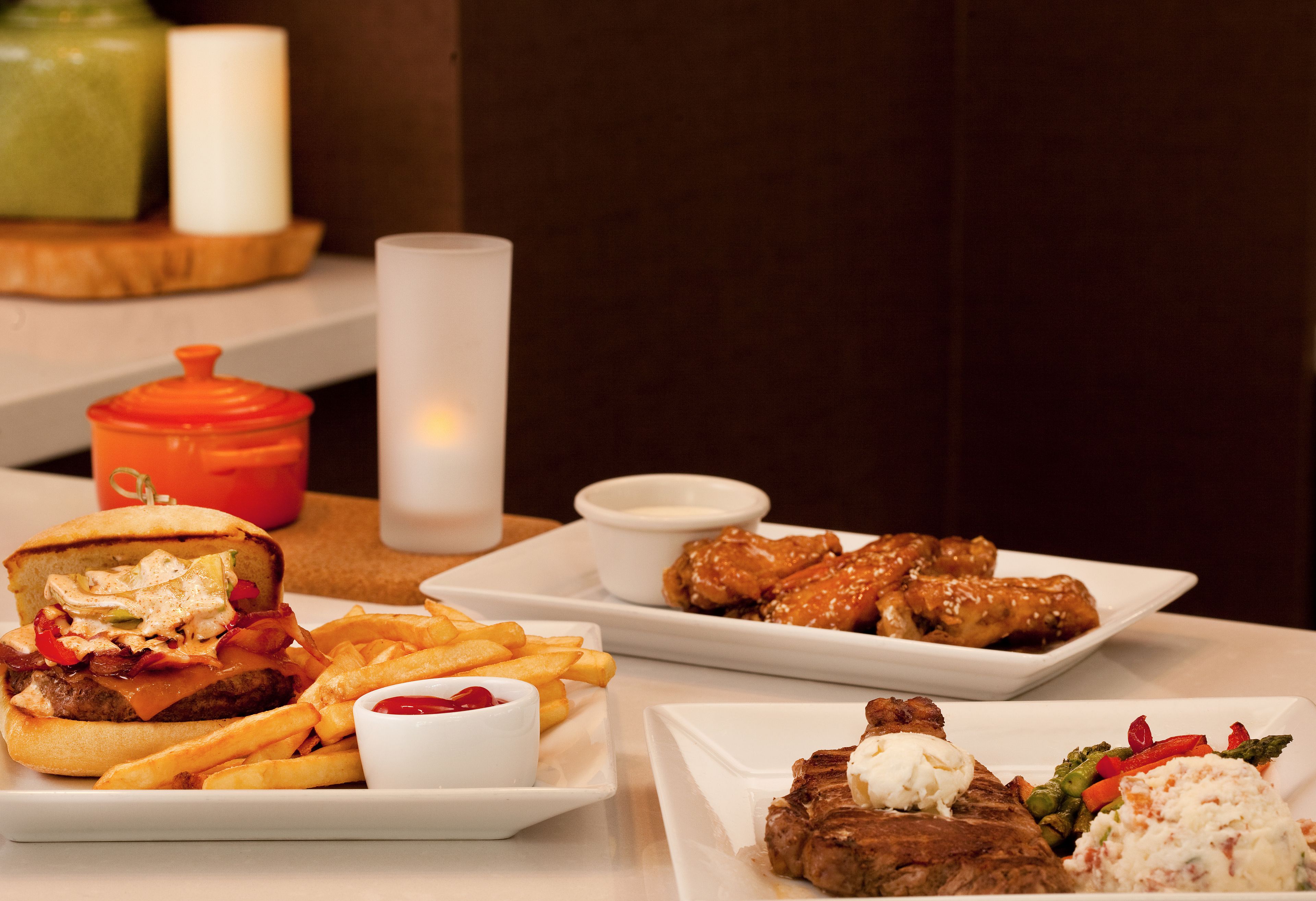 A dining table with various dishes including a burger, fries, chicken wings, and a steak with vegetables.