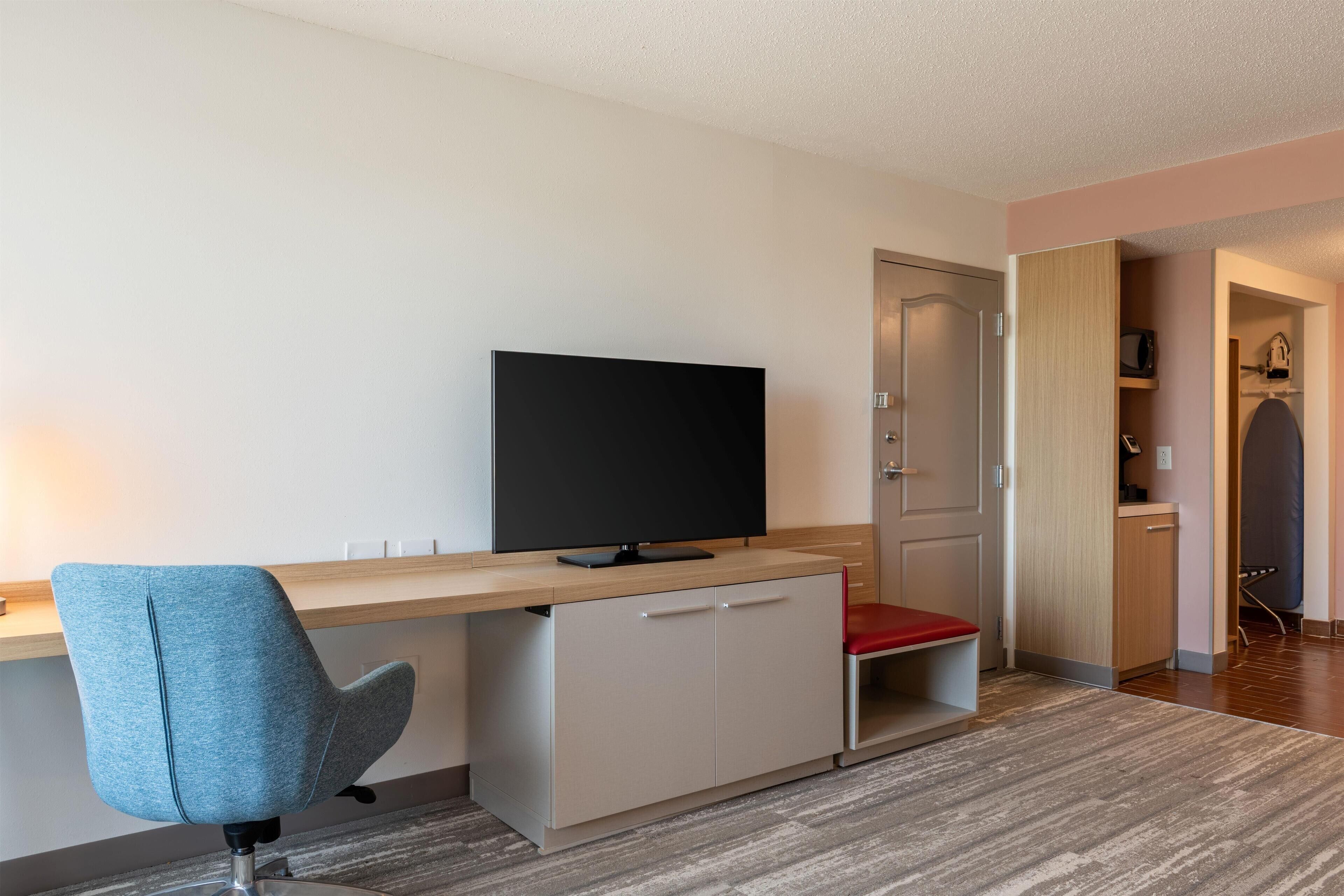 Una habitación moderna con escritorio, televisor, una silla roja y armario.