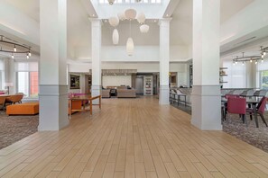 A spacious hotel lobby with a high ceiling, large windows, and a central seating area.