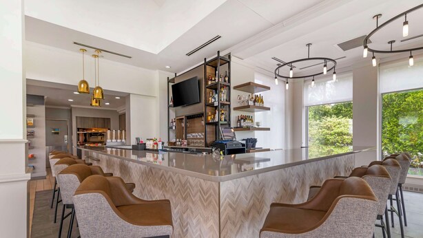 A modern kitchen with a central island, bar stools, a flat-screen TV, and wine bottles on shelves. - Hilton Garden Inn Portland Airport (Portland)