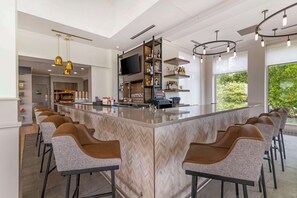 A modern kitchen with a central island, bar stools, a flat-screen TV, and wine bottles on shelves. - Hilton Garden Inn Portland Airport (Portland)