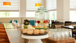 A dining area with a long table, a glass jar with fruit slices, and several granola bars on a plate. - Hilton Garden Inn Portland Airport (Portland)