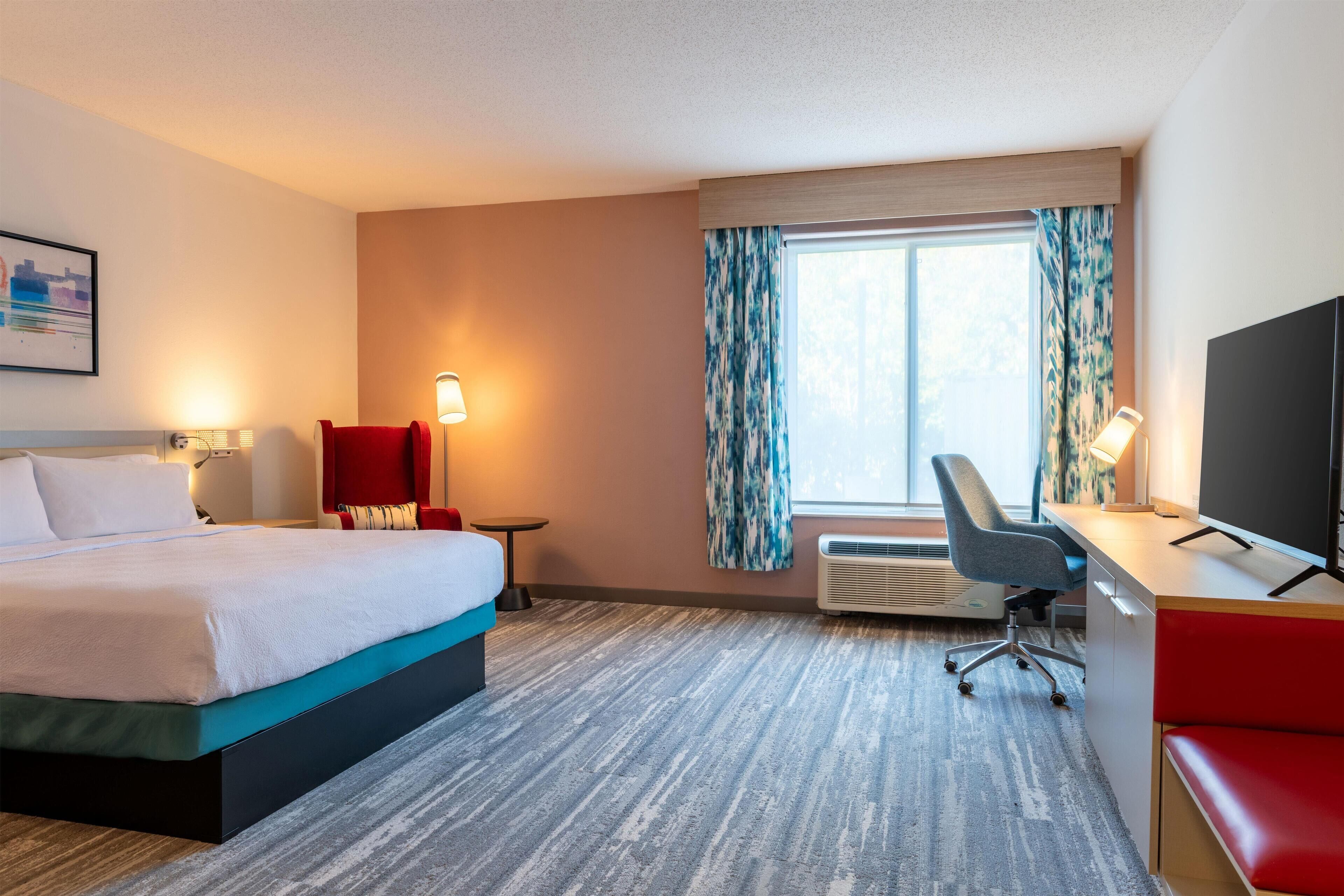 A hotel room with a bed, desk, chair, and TV.