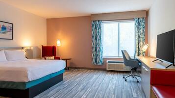 A hotel room with a bed, desk, chair, and TV.