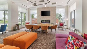 A modern hotel room with a large window, a dining area with a wooden table and chairs, and a sofa with colorful pillows. - Hilton Garden Inn Portland Airport (Portland)