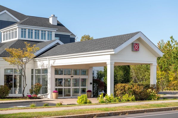 A modern building with a covered entrance, large windows, and a well-maintained garden.