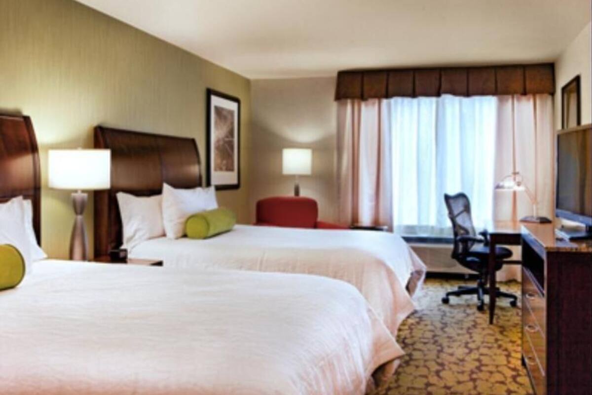 A hotel room with two beds, a desk, a chair, a TV, and a window with curtains.