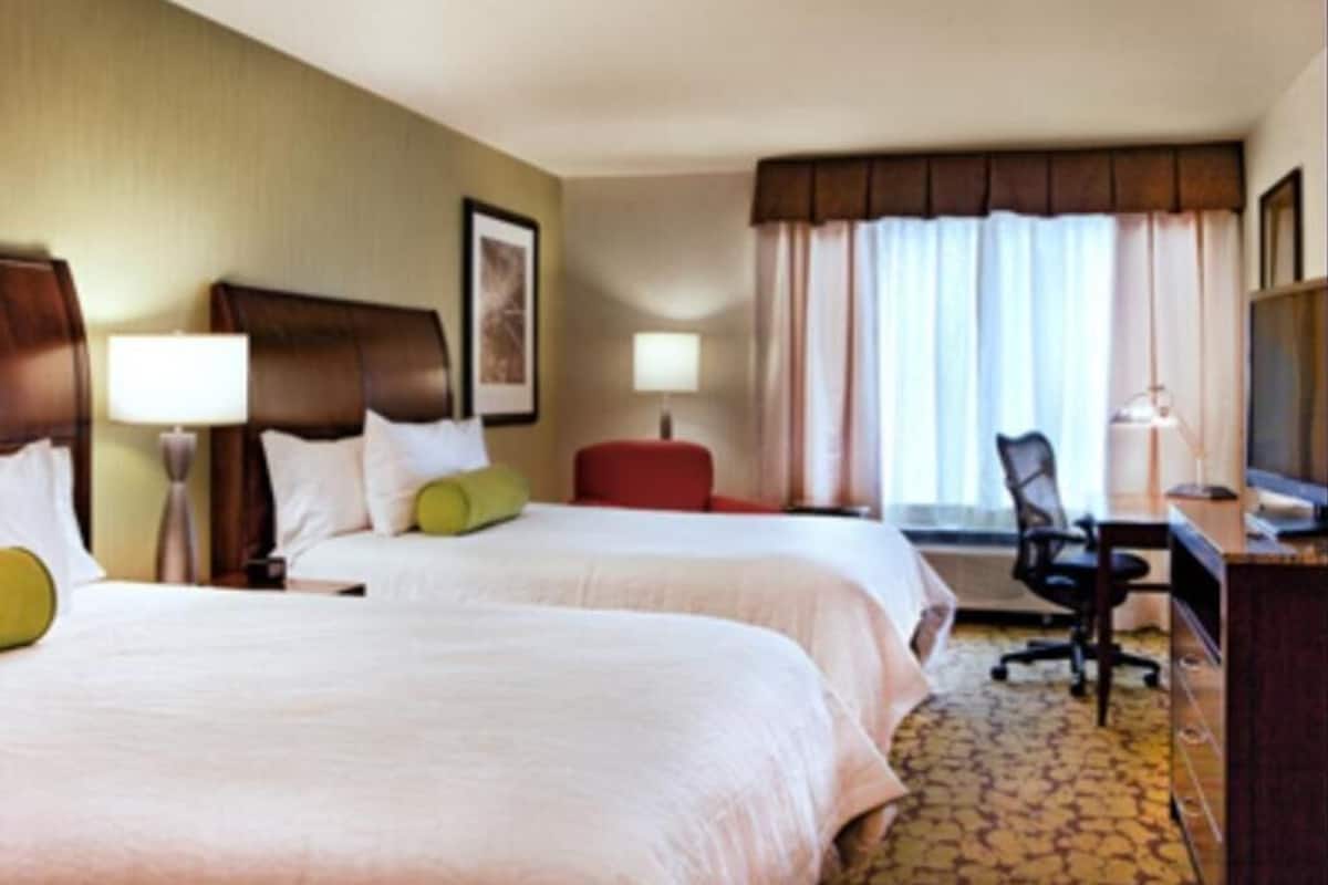 Habitación de hotel con dos camas, un escritorio, una silla, un televisor y una ventana con cortinas.