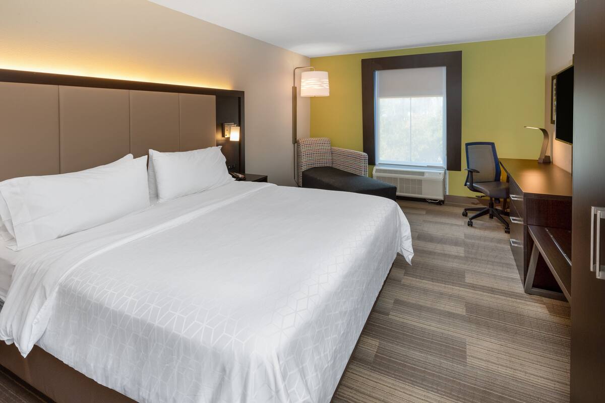 A hotel room with a large bed, a desk, a chair, and a window.