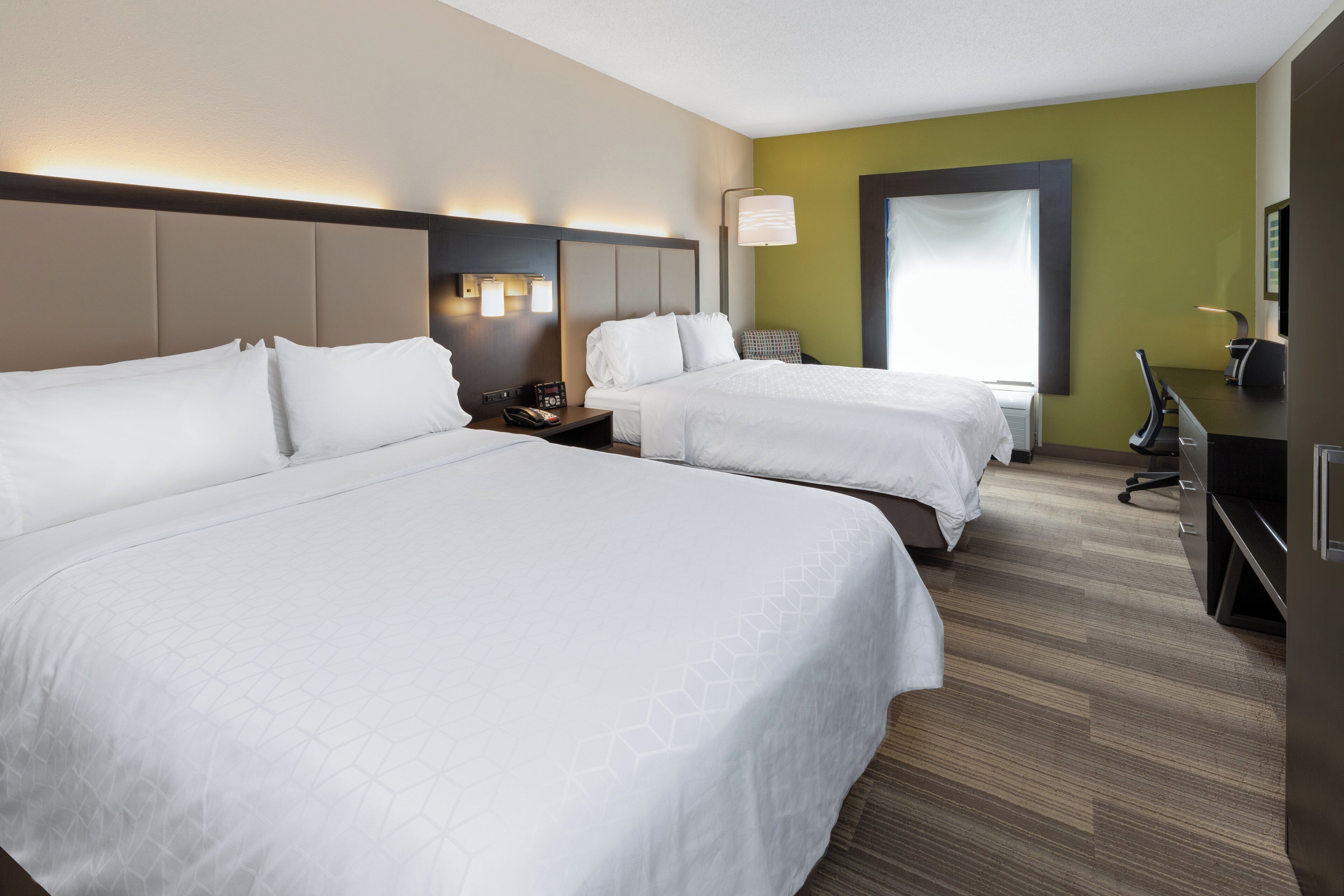 Ett hotellrum med två sängar, ett skrivbord, en stol och ett stort fönster.