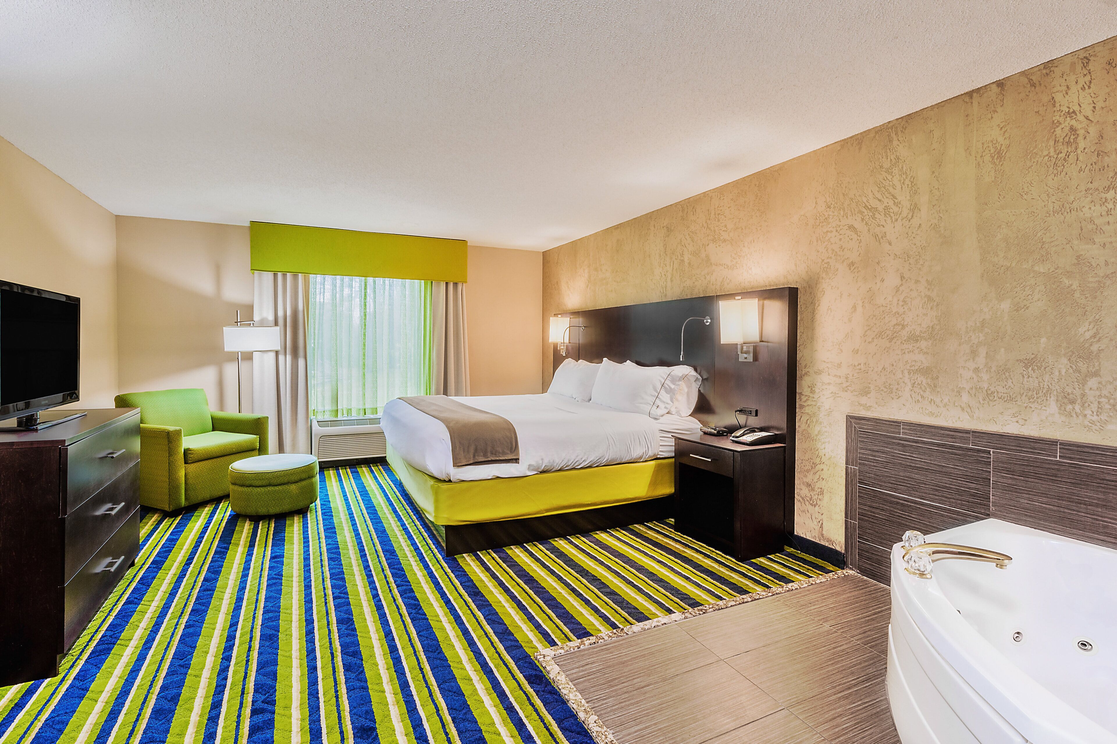 A hotel room with a bed, a television, a desk, a chair, a small table, and a bathtub.