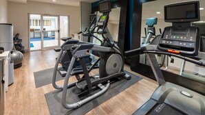 Un gimnasio con máquinas de cardio, un banco de pesas y un espejo grande.