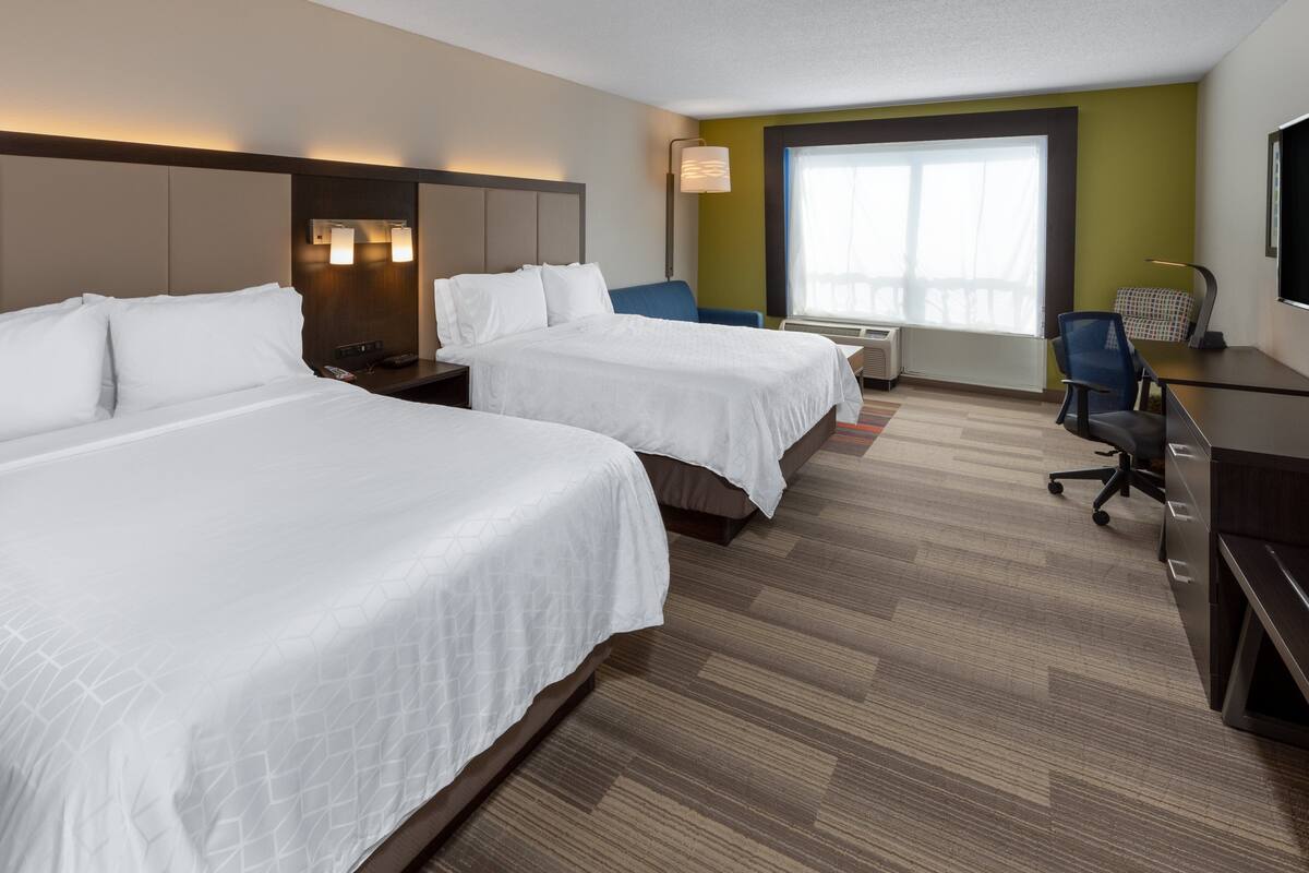 Une chambre d’hôtel avec deux lits, un bureau, une chaise et une grande fenêtre.