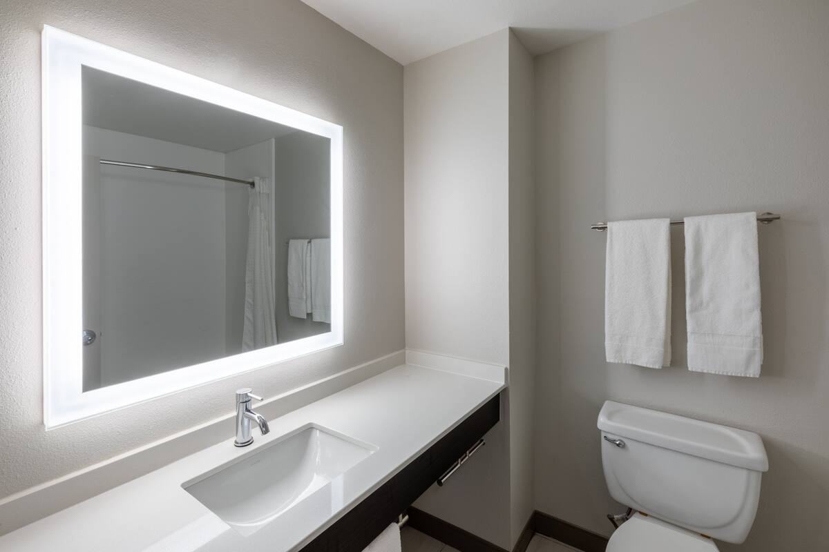 A modern bathroom with a large mirror, white sink, and toilet.