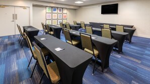 Un salón de conferencias con mesas largas, sillas, un televisor de pantalla plana y cuadros en la pared.
