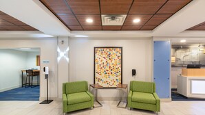 Un área de recepción con dos sillones verdes, un colorido mural geométrico, un mostrador de recepción y una cocina visible al fondo.