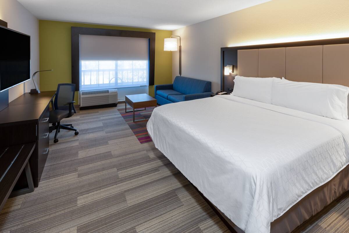 Une chambre d’hôtel avec un grand lit, un bureau avec une chaise, un canapé et un téléviseur.