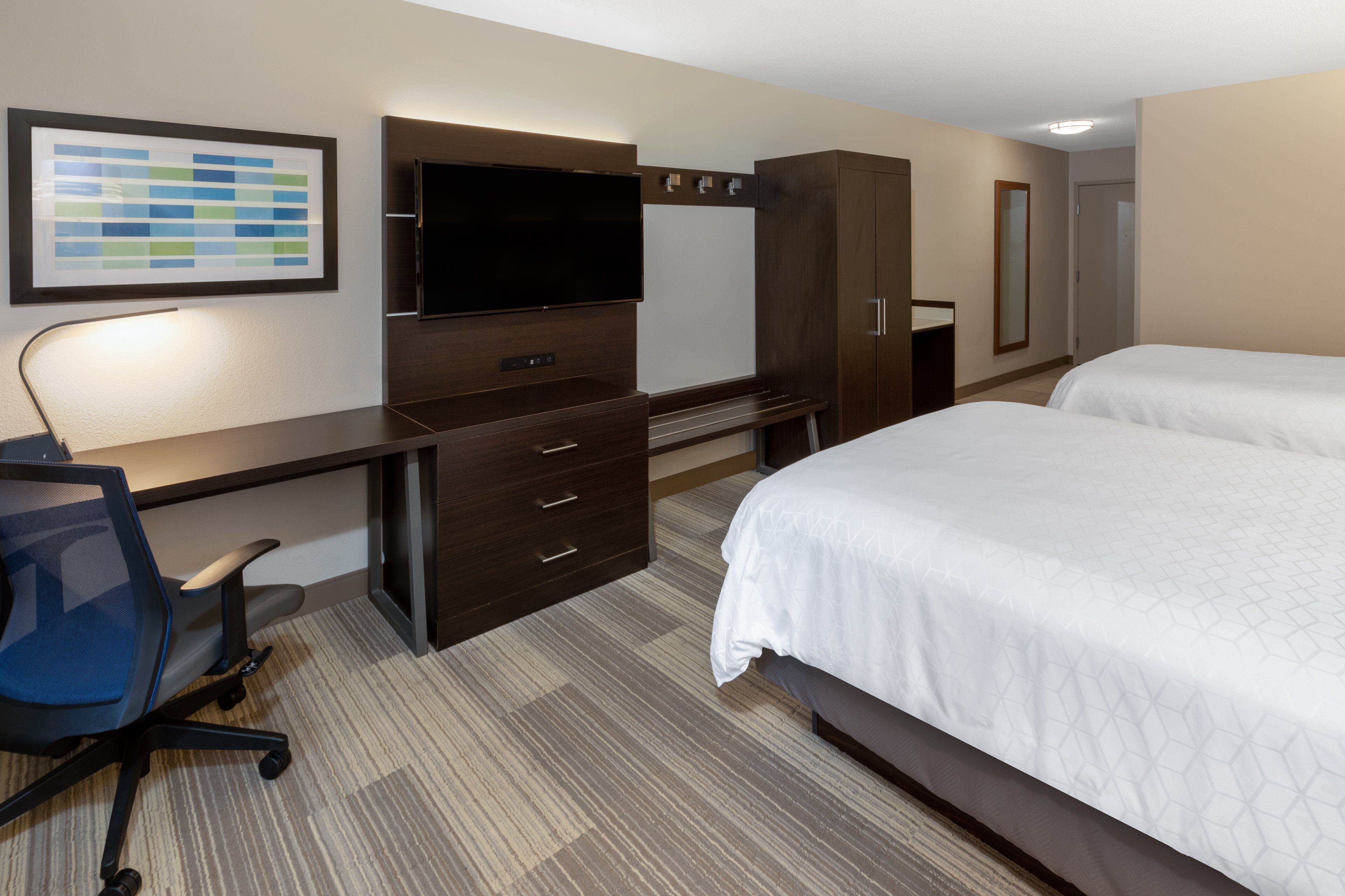 A hotel room with a desk, chair, TV, wardrobe, and two beds.
