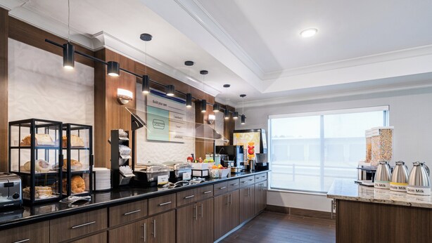 A modern kitchen area with a breakfast bar, various food items, and a coffee station.
