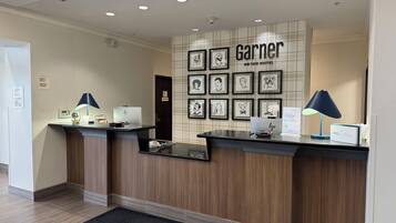 A hotel reception desk with framed artwork on the wall, a check-in counter, and a desk lamp.