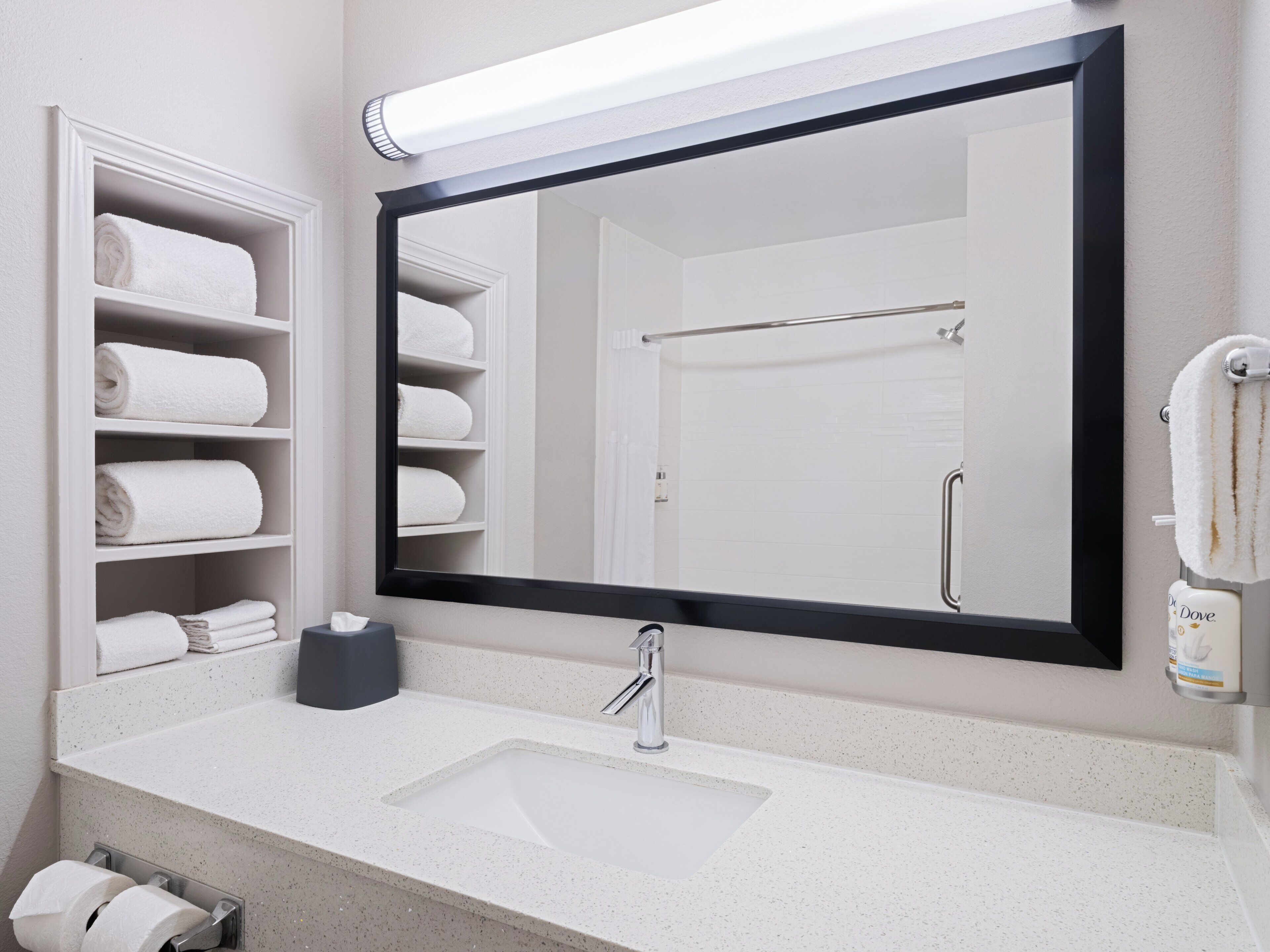 A bathroom with a large mirror, a sink, a towel rack, and a soap dispenser.
