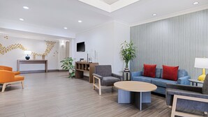 A modern hotel lobby with a reception desk, seating area, and a large window.