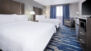 A hotel room with two beds, a TV, a desk with a lamp, a chair, and a minibar.