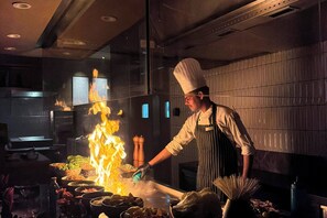 Un chef cuisinant avec des flammes sur une cuisinière dans une cuisine moderne.