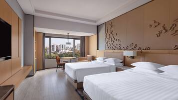 A hotel room with two beds, a TV, a desk, and a view of the city.