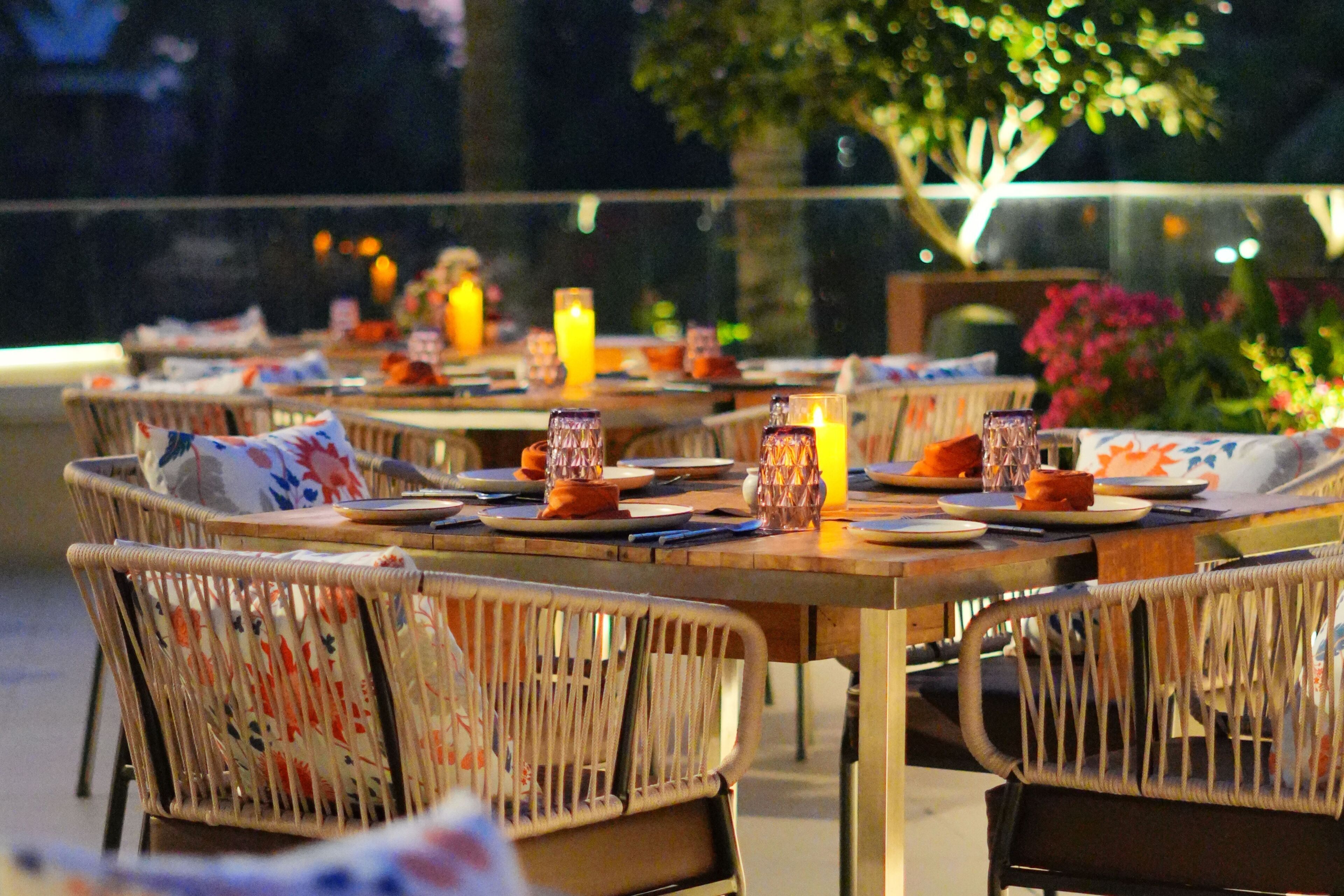 Un área de comedor al aire libre con sillas y mesas de mimbre, velas y un vaso de jugo de naranja.