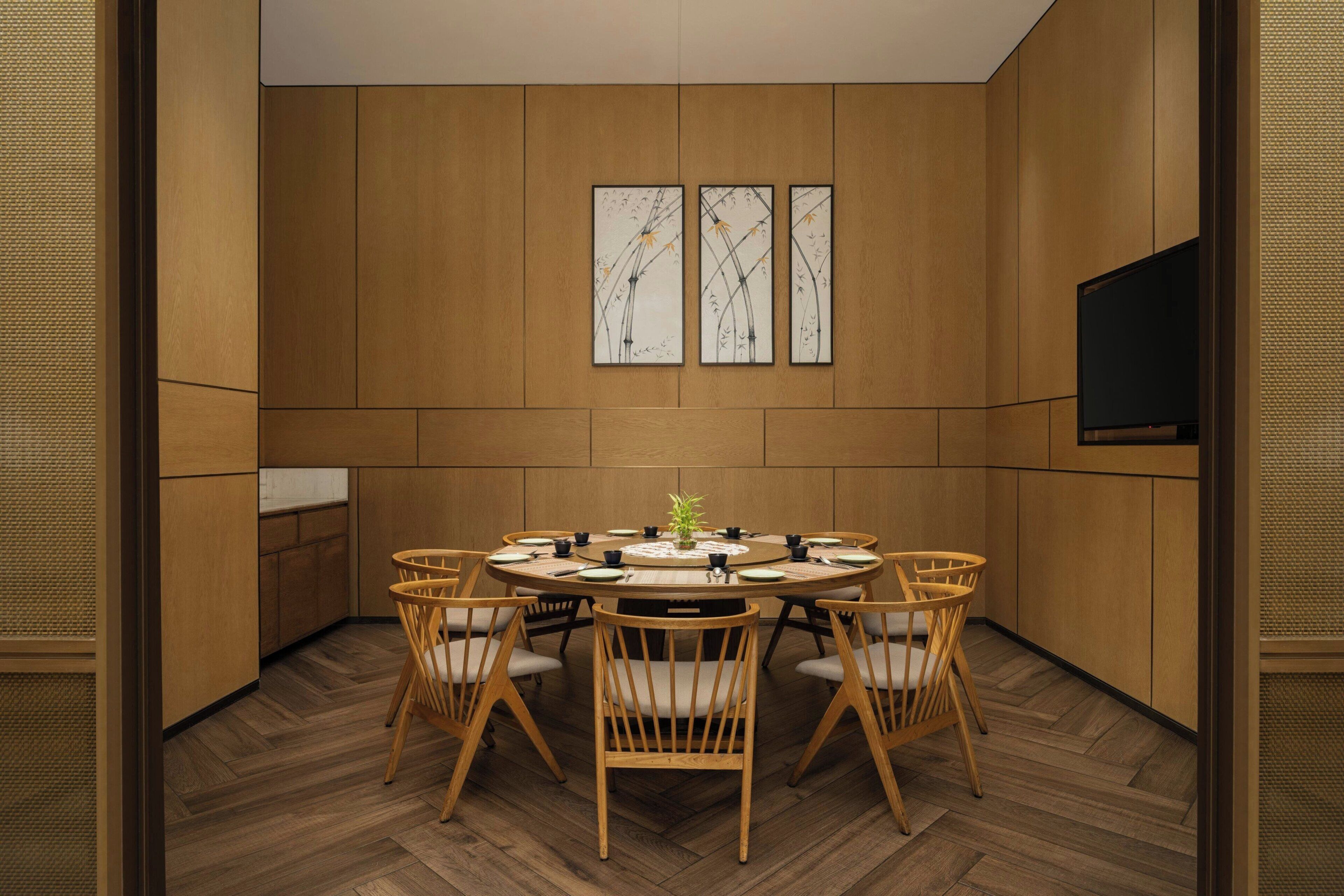 A conference room with a round table, six chairs, a flat-screen TV, and three framed artworks on the wall.