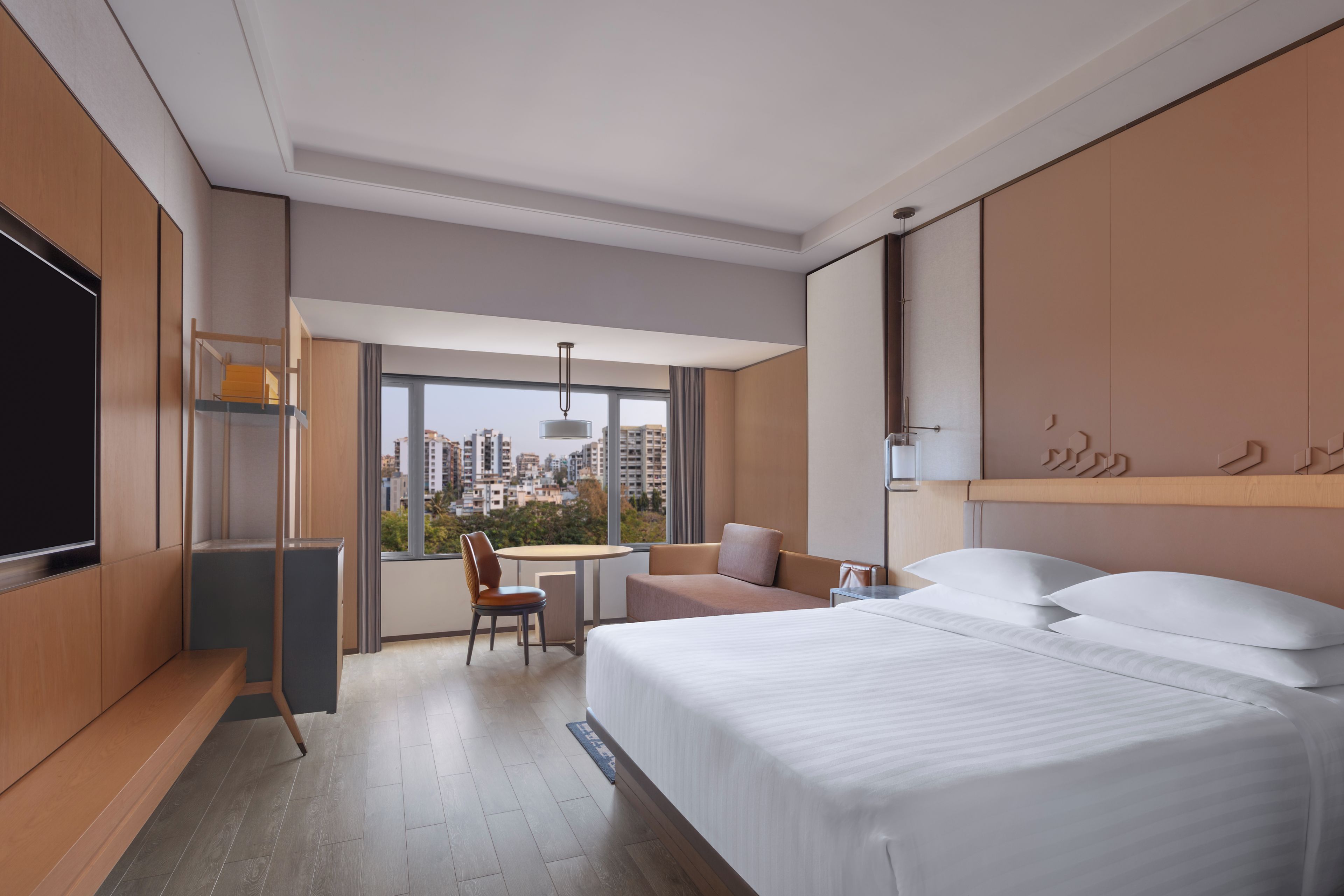 A hotel room with a bed, a desk, a chair, and a view of the city.