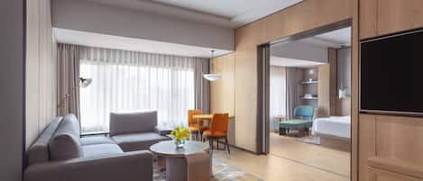 Una habitación de hotel moderna con sofá, una mesita redonda, televisor y un área de comedor con sillas y una mesa.