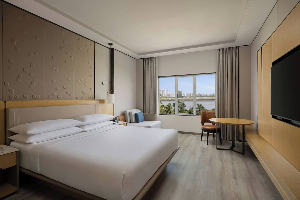 Quarto de hotel com cama grande, televisão, escrivaninha, cadeira e vista para a cidade.