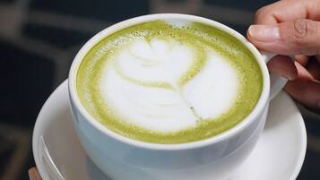 A cup of green tea latte with a heart design on the foam, held by a hand.