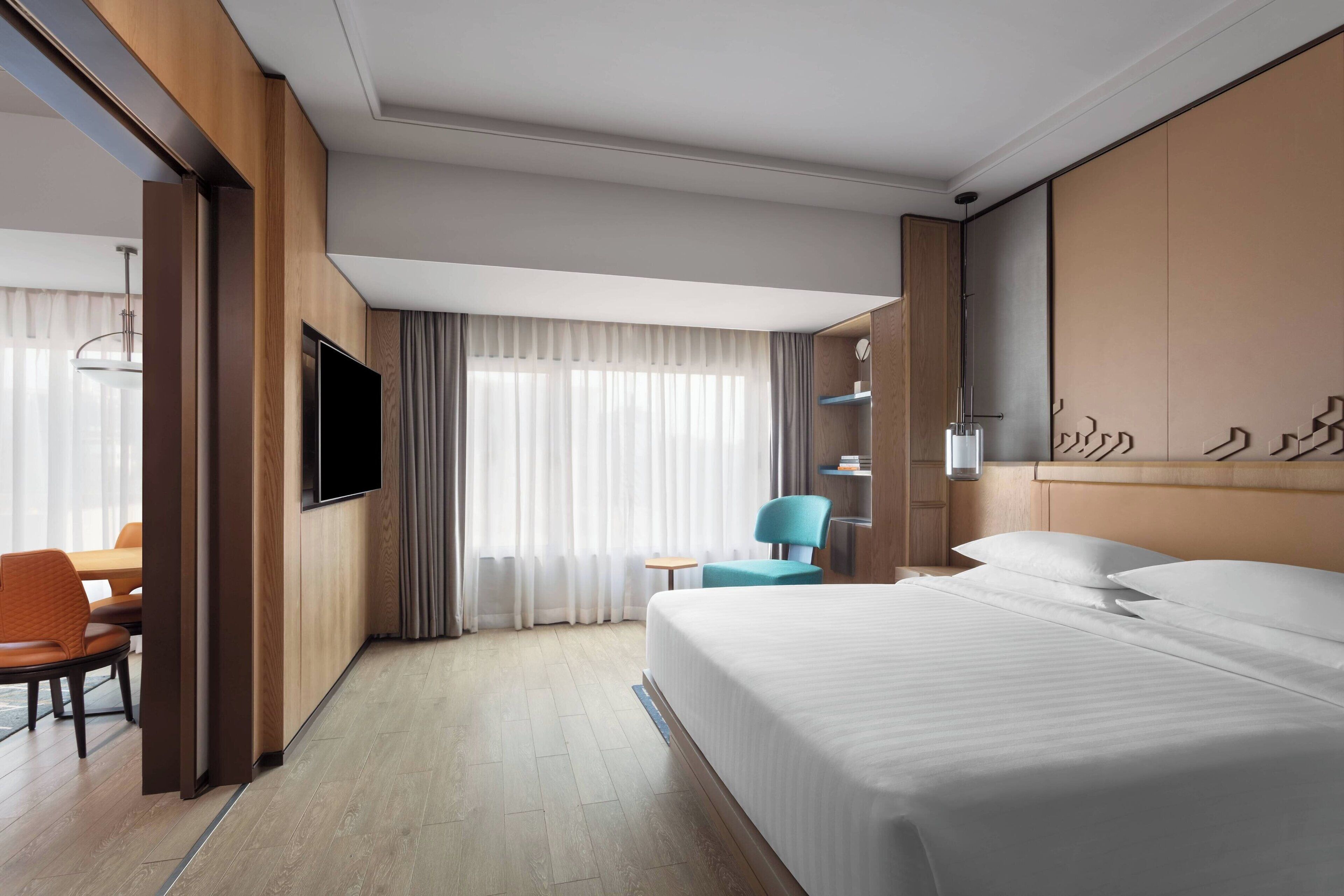 Habitación de hotel con cama, televisión, escritorio con silla y ventana con cortinas.