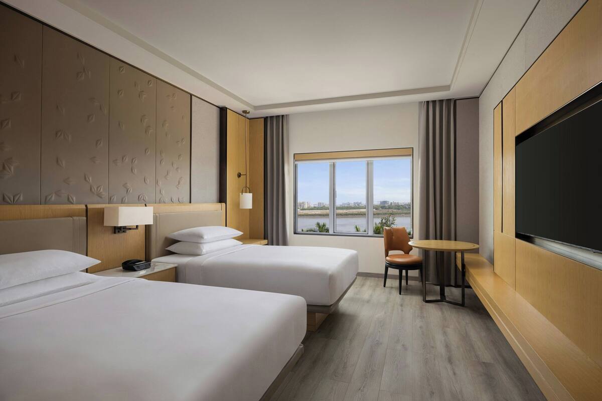 Quarto de hotel com duas camas, televisão, uma mesinha e vista para a água.
