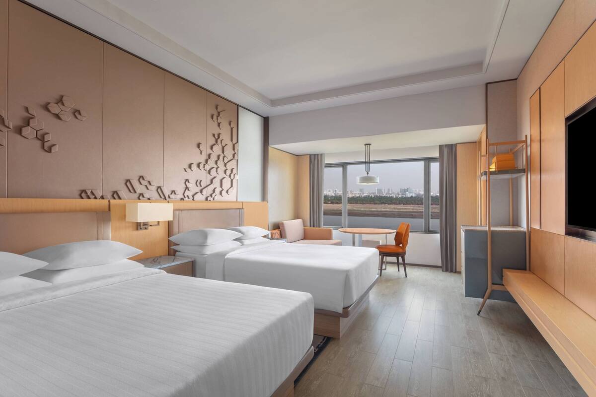 Quarto de hotel com duas camas, televisão, escrivaninha e vista para a cidade.