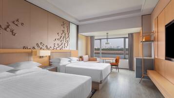 Ein Hotelzimmer mit zwei Betten, einem Fernseher, einem Schreibtisch und Blick auf die Stadt.
