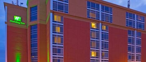 Edificio de hotel Holiday Inn con un llamativo letrero verde, amplias ventanas y fachada de ladrillo.