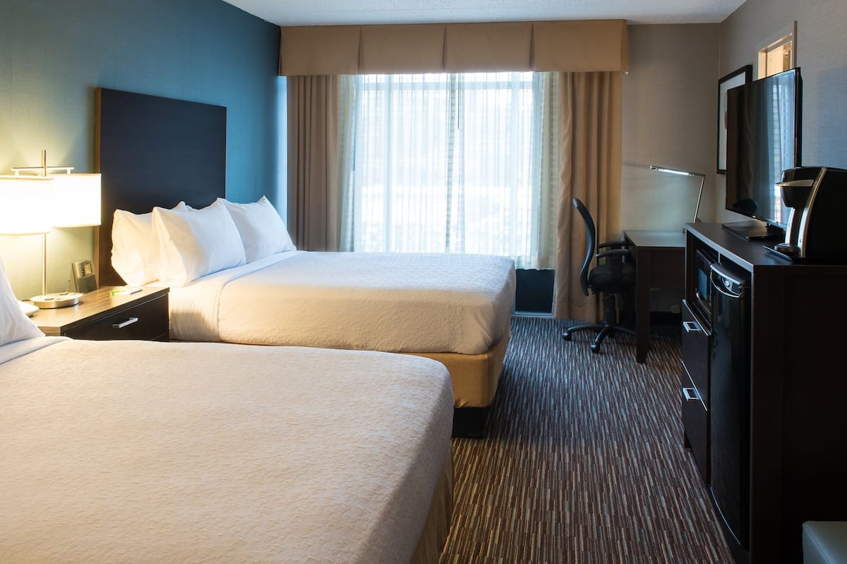 Ein Hotelzimmer mit zwei Betten, einem Schreibtisch mit Lampe, einem Fernseher und einer Minibar.